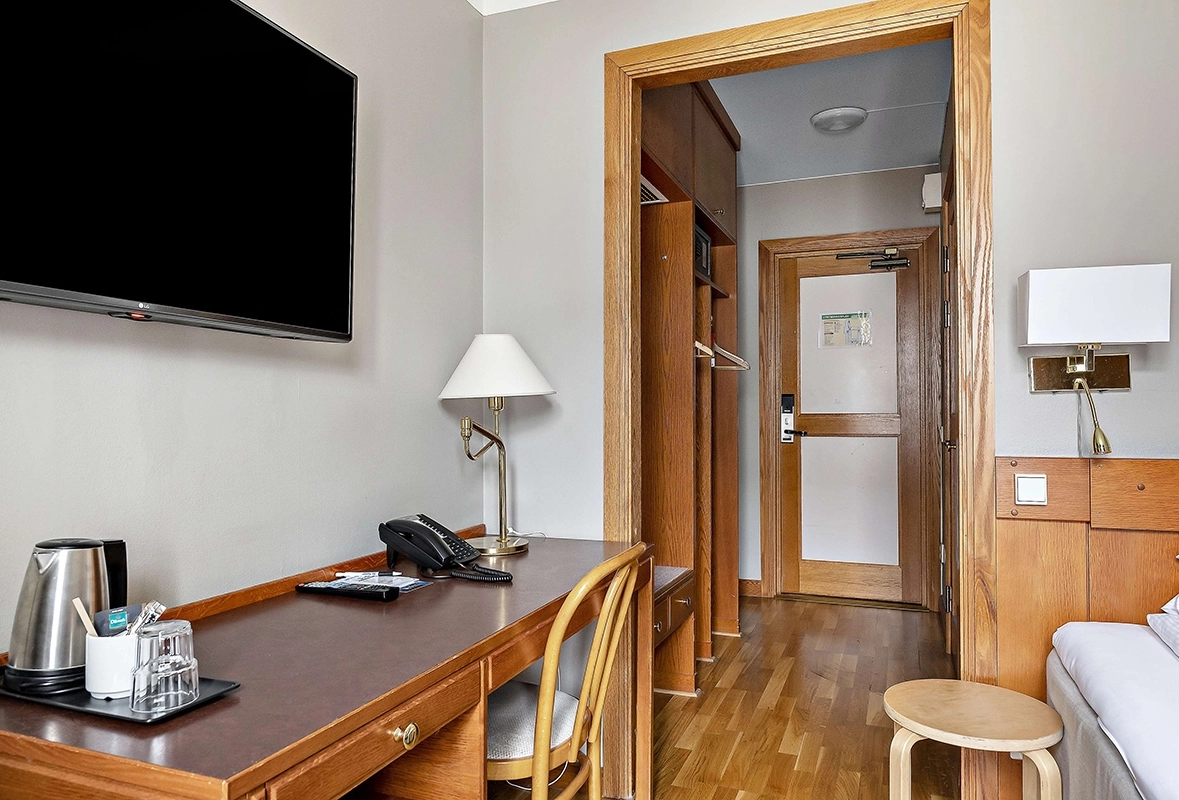 Ett enkelrum på Best Western Gustaf Wasa Hotel. Ett skrivbord med tillhörande stol. En pall bredvid sängen och en tv på väggen.