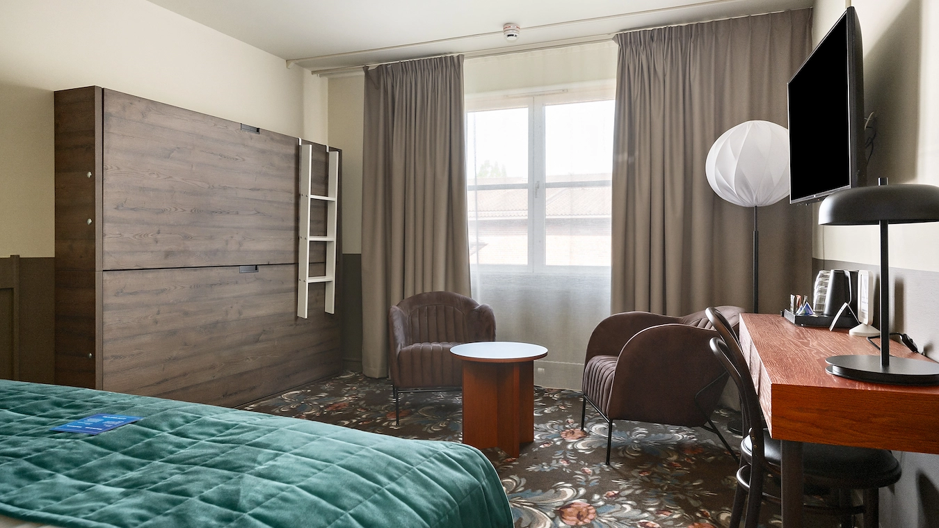 En icke-utfälld våningssäng, en sittgrupp, ett skrivbord med stol och en tv upphängd på väggen. Den nedre delen av en stor säng.