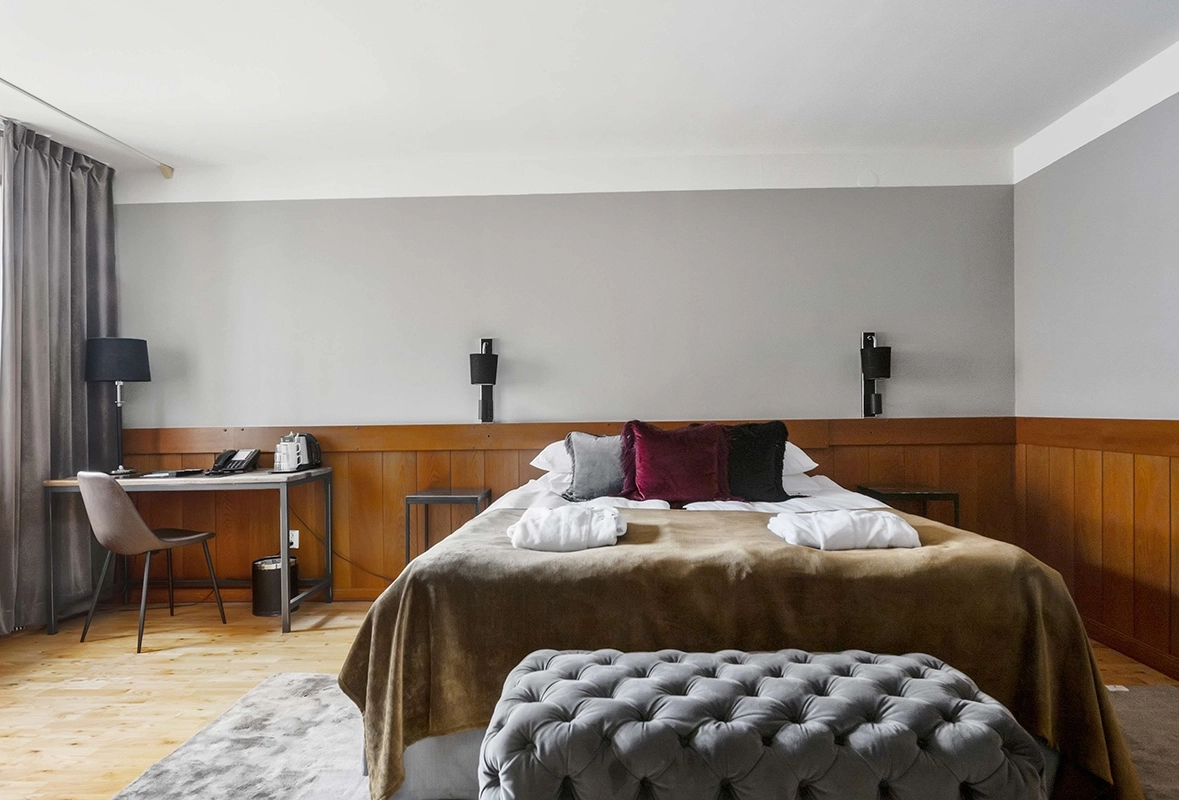 En lyxig säng med en sittdyna vid fotändan. Ett skrivbord med tillhörande stol.