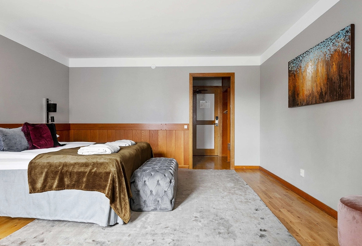 En lyxig säng med en sittdyna vid fotändan. En målning på väggen mot sängen.