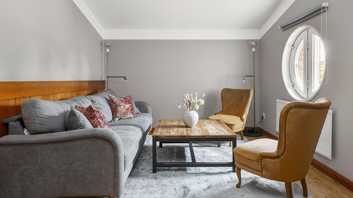 En soffa och två fåtöljer runt ett lågt bord på en matta. Ett fönster med en mörkläggningsgardin.