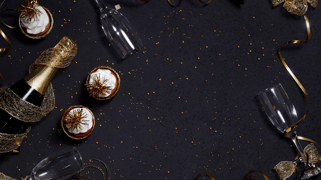 En inzoomad bild av ett svart bord med guldglitter, champagneglas, och muffins på.