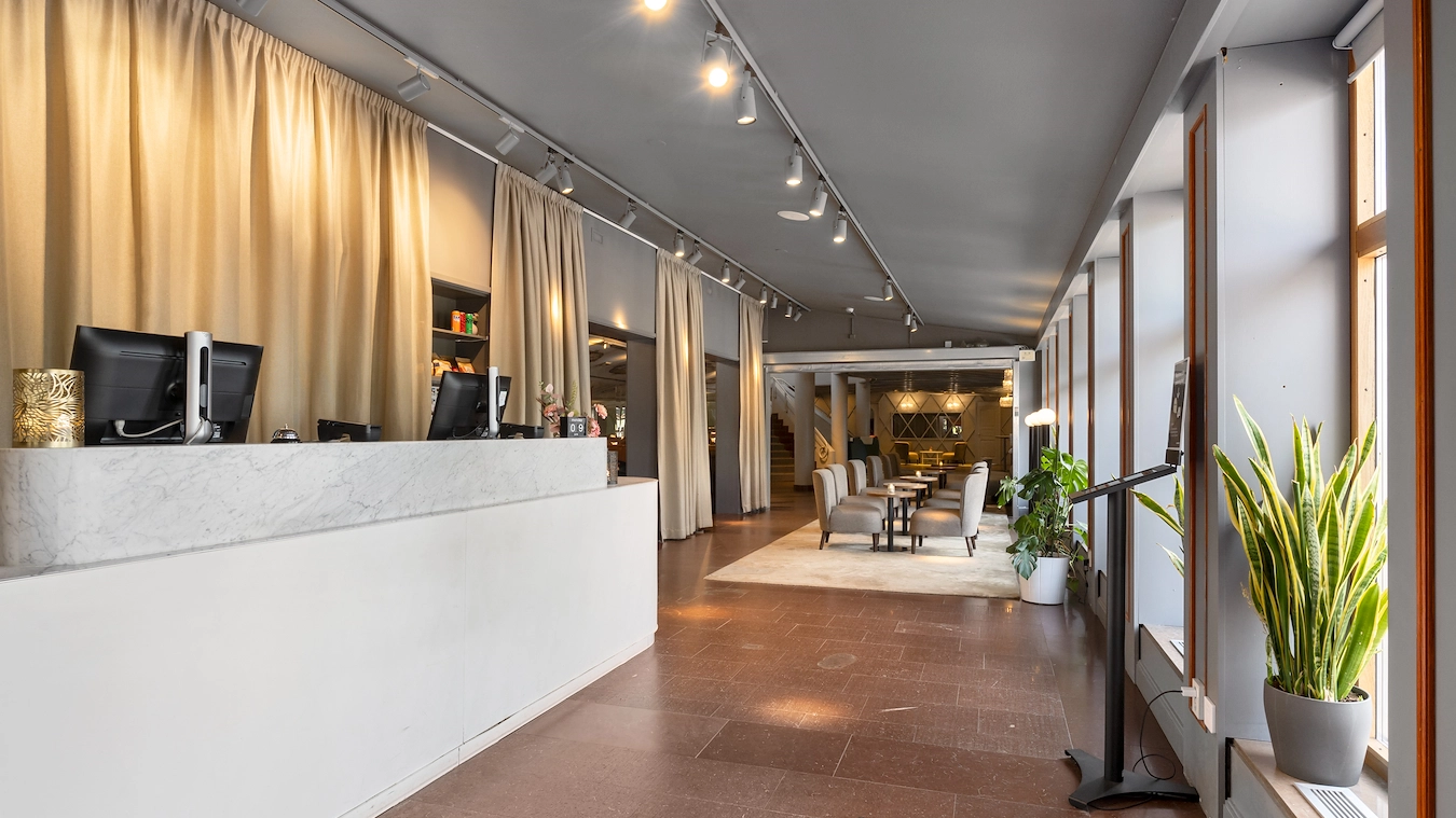 Hotellobbyn på Best Western Gustaf Wasa Hotel i Borlänge. Stor yta med sittgrupper i bakgrunden och en grå receptionsdisk i förgrunden