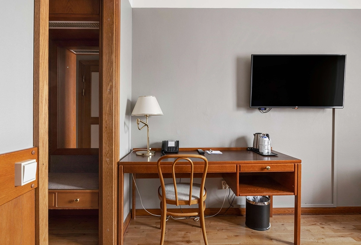 Ett standardrum med ett skrivbord och tillhörande stol samt en tv som hänger på väggen.