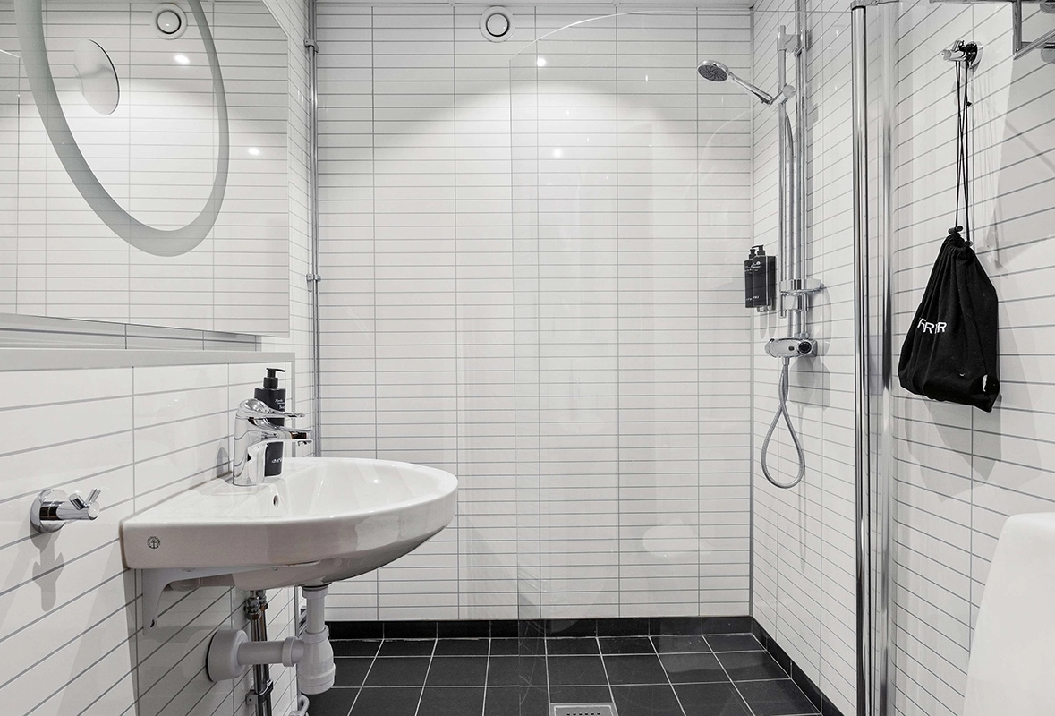 Ett vitt badrum med svart golv. Handfat, spegel och dusch syns i bild.