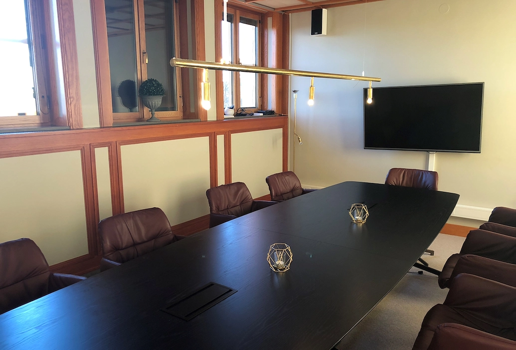 En närbild på det svarta träbordet från Styrelserummet på Best Western Gustaf Wasa Hotel. Runtom bordet står skinnstolar och en tv pryder väggen bak i rummet.