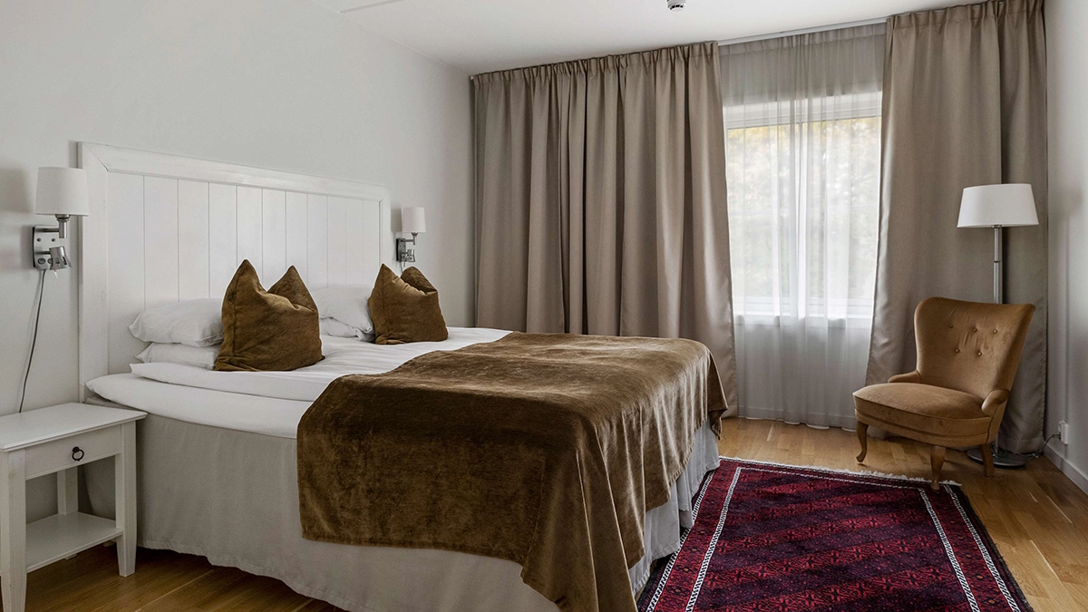 Ett superior dubbelrum med en dubbelsäng, ett fönster och en fåtölj med en lampa bakom.