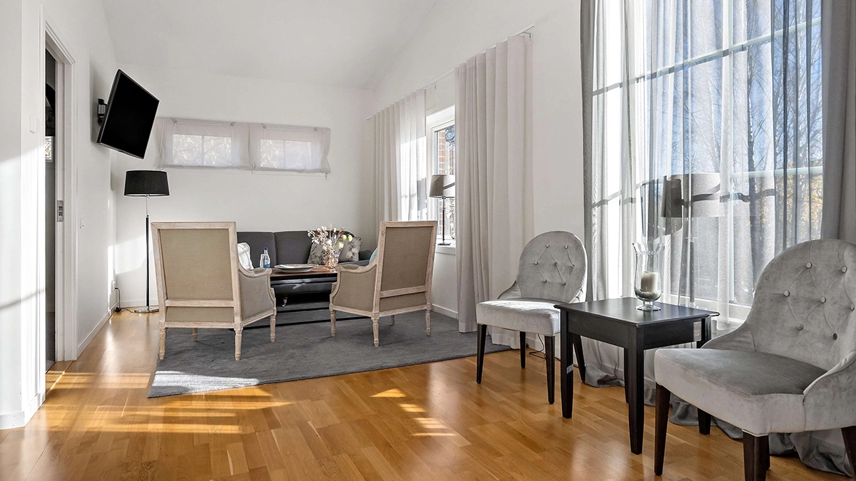 Två fåtöljer och ett litet bord vid ett fönster. Längre bak i bilden står ytterligare två fåtöljer och en soffa. På väggen hänger en tv.