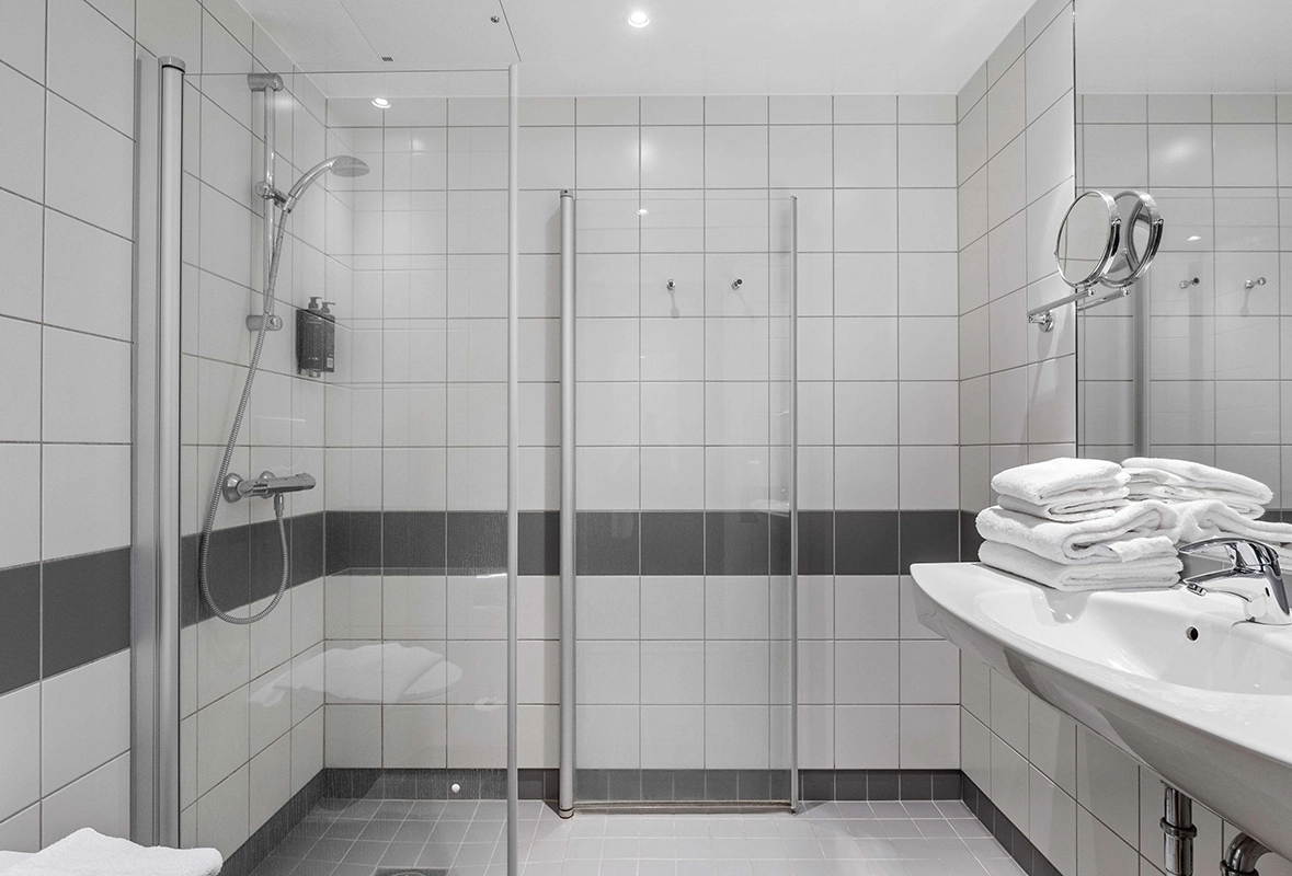 Ett stort vitt badrum med svarta detaljer. Till vänster en dusch och till höger ett handfat.