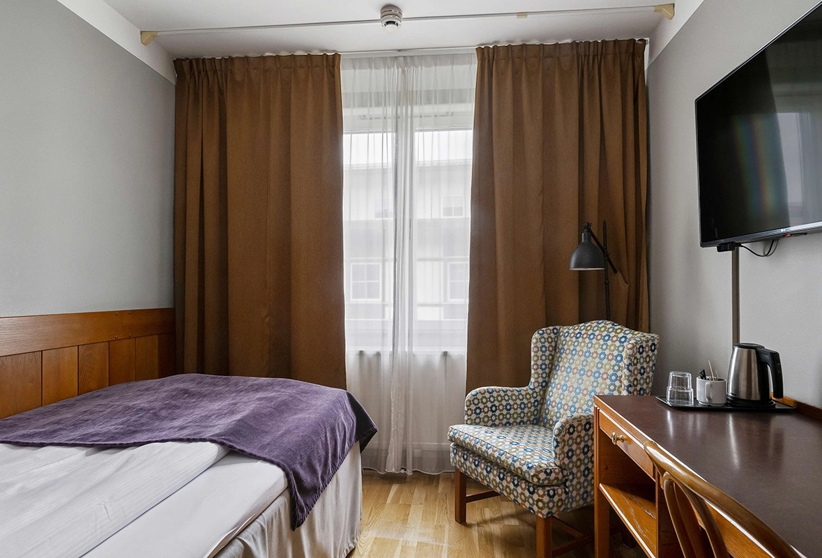 Ett enkelrum på Best Western Gustaf Wasa Hotel. En färgglad fåtölj bredvid skrivbordet och fönster vid fotändan av sängen.