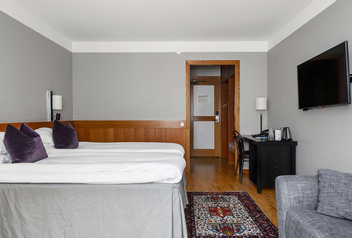 Ett familjerum med en dubbelsäng, en liten soffa, ett skrivbord och en tv som hänger på väggen.