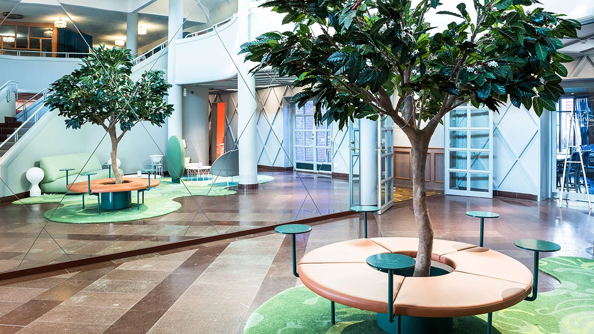 Lobbyn på Gustaf Wasa Hotell. Öppet landskap, sittgrupper och träd. I bakgrunden en trappa.