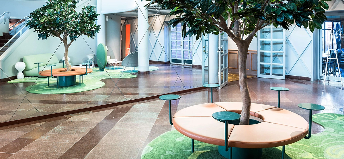 Lobbyn på Gustaf Wasa Hotell. Öppet landskap, sittgrupper och träd. I bakgrunden en trappa.