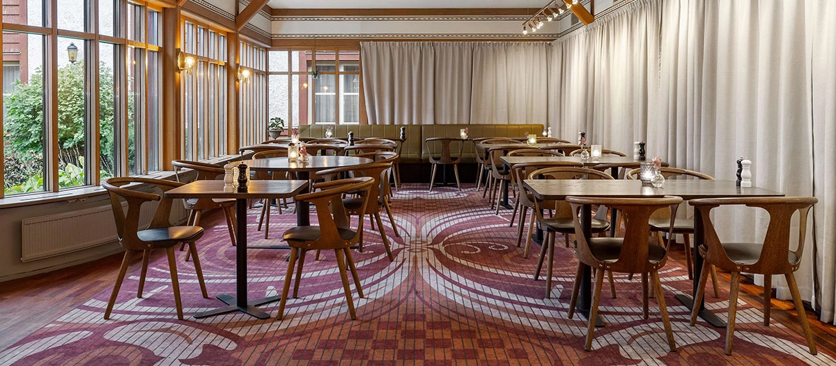 Ett flertal stolar och bord i mörkt trä uppställda i lunchmatsalen på Best Western Gustaf Wasa Hotel.