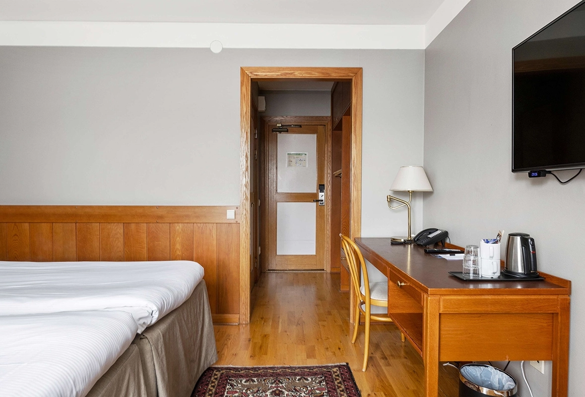 Ett standardrum med en dubbelsäng, ett skrivbord med en stol och en tv som hänger på väggen.