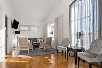 Två fåtöljer och ett litet bord vid ett fönster. Längre bak i bilder står ytterligare två fåtöljer och en soffa. På väggen hänger en tv.